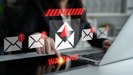 A business professional interacts with a laptop, focusing on warning email notifications. The image...