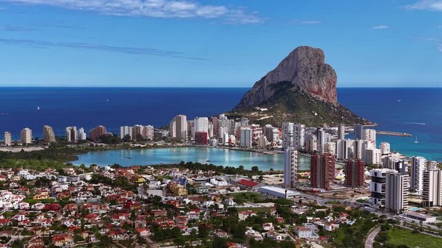 Panoramic aerial view of Calpe, Spain, featuring the iconic Penon de Ifach limestone rock, turquoise lagoon, urban skyline and Mediterranean coastline under clear blue sky