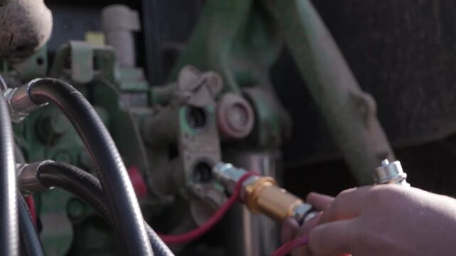 Farmer Connecting Grader Hydraulics to Tractor. Close view of farmer connecting hydraulic lines from grader to tractor