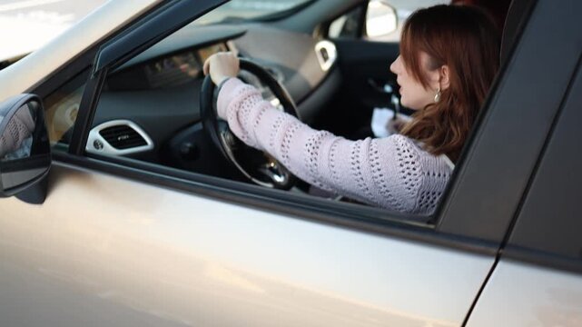 Nervous young woman driving car for first time during lesson tight grip on steering wheel while instructor writes notes focused beginner gaining confidence in real road training