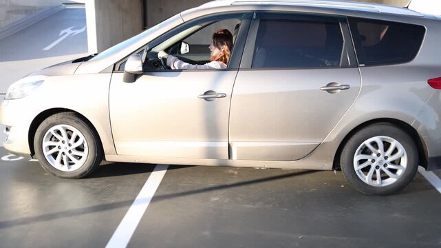 Young woman carefully drives a car across open parking area during driving lesson keeping steady hands on the wheel while instructor observes her actions and progress