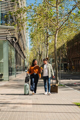 Obraz premium Two joyful travelers stroll side by side, pulling their luggage with excitement as they explore new adventures while enjoying a sunny day filled with laughter and companionship in a vibrant city.