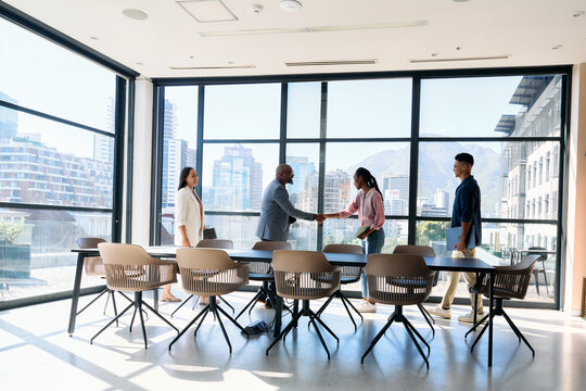Confident business professionals shaking hands near team in boardroom at office during daytime