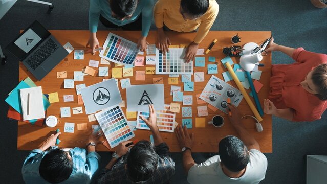 Top down view of smart designer explain and brainstorming idea for logo design and writing concept. Aerial view of business people discuss and talking while using sticky notes sharing idea. Symposium.