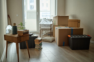 Wide shot of packed moving boxes, storage bins, books, chair, and decor filling empty apartment, suggesting relocation and home setup. Ideal for moving services, real estate, downsizing © Seventyfour