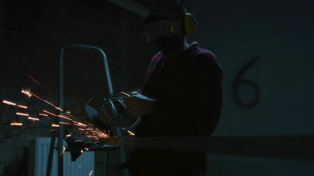 Male industrial worker or construction worker cuts metal with a angle grinder. Man uses metal saw or grinder at factory, Grinding Metal. Close-up sparks flying, manufacturing plant, cutting metal