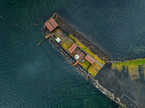 Aerial view of Skarungen basecamp featuring traditional wooden cabins on a rocky pier surrounded by dark blue water in Kabelvag, Nordland, Norway.