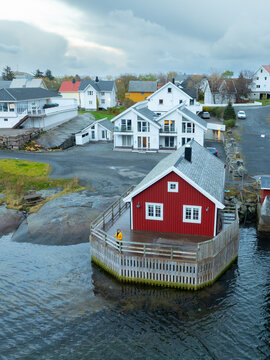 Aerial view of May's Apartments and Maybua with a woman in a yellow jacket on the deck of a red cabin by the water in Reine, Nordland, Norway.