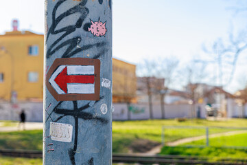 Red Arrow Sticker on Graffiti-Covered Pole Pointing Left in Urban Street Scene © Olga