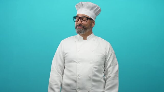 Man chef middle age hispanic with grey hair beard and glasses in white uniform and hat smiling in turquoise studio; confidence expertise.