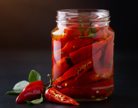 A red chili pepper, spicy and fresh, is placed in a glass jar on a black background, showcasing a vibrant Calabrian hot pepper ingredient. This preserved food is healthy, organic, and a natural vegeta