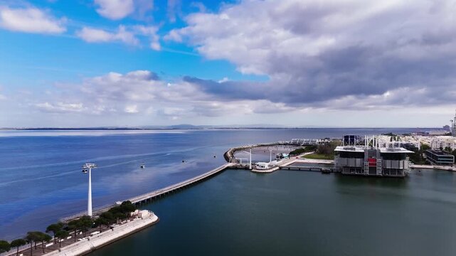 Aerial view of cable cars over Tagus river and waterfront under dramatic clouds. Lisbon, Portugal
