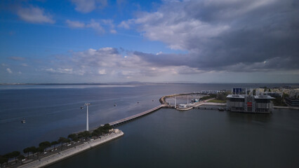 Fototapeta premium Aerial view of cable cars over Tagus river and waterfront under dramatic clouds. Lisbon, Portugal