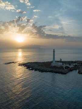 Aerial view of the Punta Sottile lighthouse on the rocky coast during a golden sunset with sunbeams through the clouds Favignana, Sicilia, Italy.