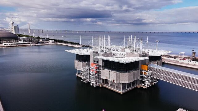 Aerial view of Oceanario de Lisboa building over Tagus river in Parque das Nacoes under a cloudy sky
