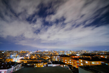 Fototapeta premium View of clouds in the dark sky over typical turkish residential buildings with warm illumination and illuminated windows in Istanbul, Turkey at night - wide angle