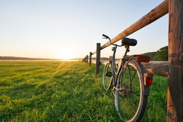 Naklejka premium Bicycle Parked by a Wooden Fence During Sunrise in a Grassy Field