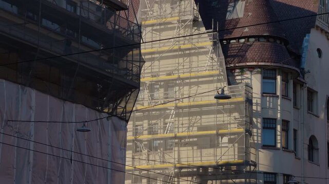 Facade restoration with scaffolding at dusk. Cinematic view of historic building with repair work underway. Urban scene depicting detailed stonework being restored amid sunset glow and scaffolding