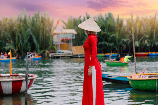 Woman in red ao dai standing by river in hoi an, vietnam at sunset. Concept travel tour coconut bamboo boats