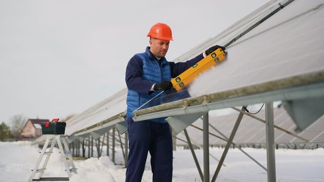 Engineer checking solar panels installation with level tool in winter