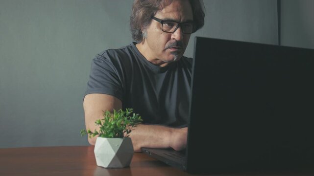 Real-life scene of a businessman checking financial data on a laptop while sitting at a desk. Natural light, authentic working moment. Not AI generated, real human activity.