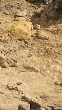 A rocky landscape shows various sizes of stones and soil. The scene captures the texture of the ground in a dry area. Sunlight highlights the colors of the rocks and earth.