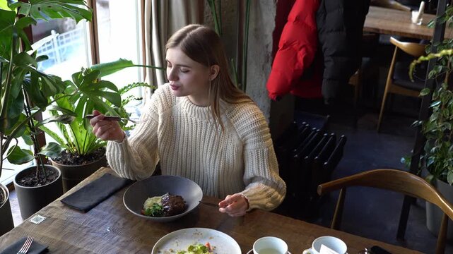 young woman with fork and knife cuts tender veal meat in cafe, girl eats beef steak and mashed potatoes in restaurant