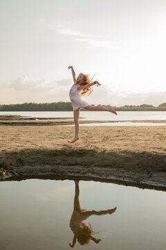Beautiful little girl jumps on the sand on the river bank. Little ballerina girl is dancing on the nature. Kid and child on vacation. Selective focus