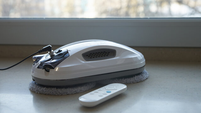 An oval-shaped robotic vacuum window cleaner and remote control lie on the windowsill.