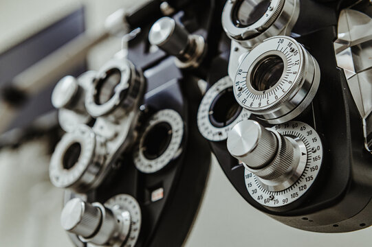 Low angle view of medical phoropter vision equipment. Upward looking perspective of an ophthalmic refractor showing various knobs, dials, and lens openings.