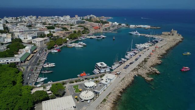 Panoramic drone shot of the historic Mandraki port in Rhodes, Greece. Featuring the three medieval windmills, Saint Nicholas Fort and the iconic deer statues under a clear blue sky. Version 2.