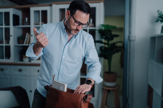 Busy man packing his leather messenger bag, preparing for work or travel, organizing daily essentials at home