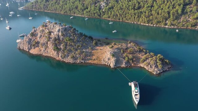 Aerial view of megayacht moored to rocky islet of Bybassios with teal water reflection, Orhaniye, Marmaris, Turkey
