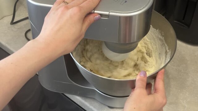 Silver stand mixer whisk attachment rotating and mixing dough in a metal bowl held by a woman. baking at home, culinary hobby, kitchen equipment.