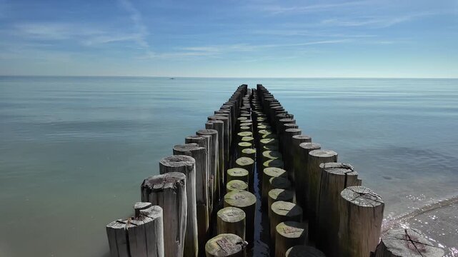 Wooden pier on the beach. Wooden breakwater posts leading into calm sea, symmetry, clear sky, minimal coastal landscape