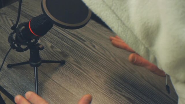 Close up of unrecognizable person talking into a studio microphone. Hands gesturing vigorously during a podcast recording or vlog session on a wooden table