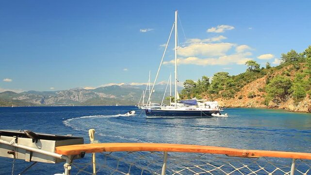 View from boat deck of a large sailboat anchored in Gocek cove with speedboat wake and mountain backdrop, Mugla, Turkey