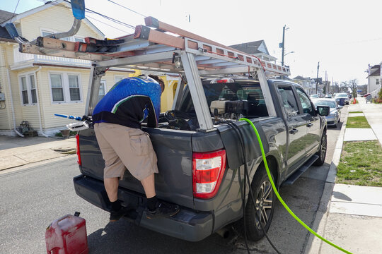 Handyman standing on his pickup truck and looking into bed with ladders on top and hoses coming from bed