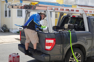 Handyman standing on his pickup truck and looking into bed with ladders on top and hoses coming from bed © ALAN