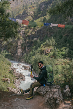 Trekker Resting by Mountain River with Prayer Flags in the Himalayas