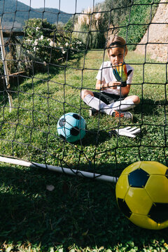 Young girl goalkeeper putting on gloves in backyard soccer goal