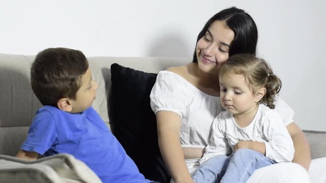 A young mother sits and talks with her children about supportive parenting and family communication at home.
