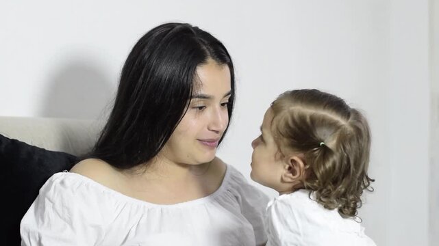 A young mother talks and plays with her little girl on the sofa, patient parenting and emotional connection at home.