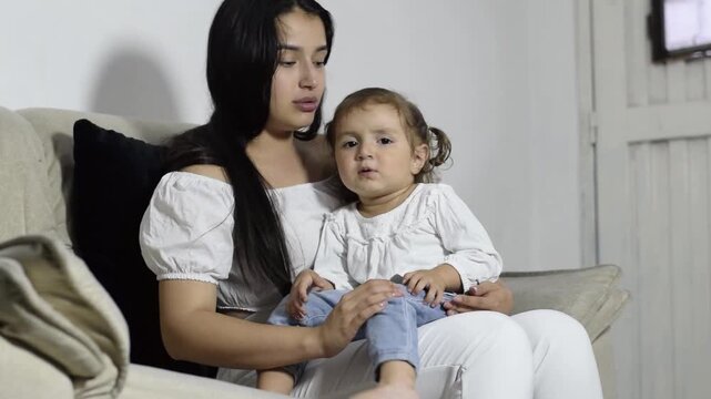 A young Latina mother talks to and explains things to her young daughter while showing her affection and being patient with her.
