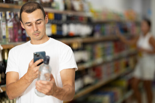 Male shoper using smartphones to scan barcodes on bottles of alcoholic beverages