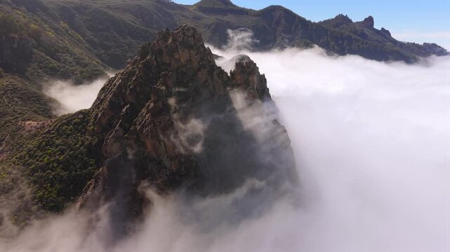 Stunning aerial view of the Roque Grande rock formation emerging from a sea of clouds. A beautiful, mystical landscape in Gran Canaria