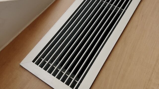 White floor air vent grille installed on a wooden floor, close up, indoor ventilation detail. 