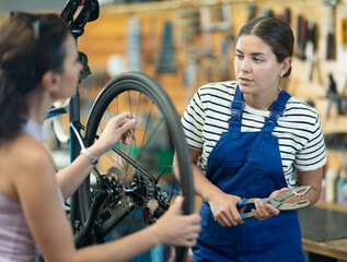 Obraz premium Young woman bicycle repair service worker in uniform advises female client