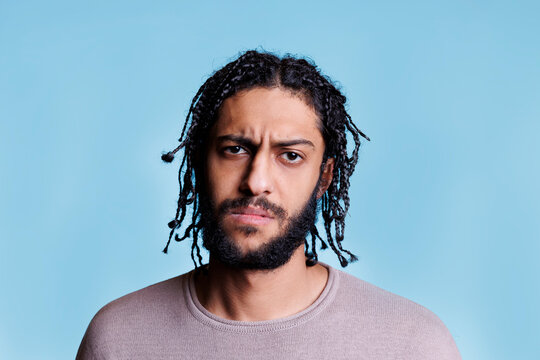 Arab confused man frowning eyebrows and looking at camera. Young adult arabian brunette person with braided hairstyle with unsure facial expression close up studio portrait