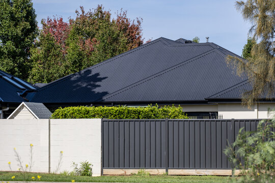 Modern Australian residential house featuring a dark corrugated metal roof and matching metal slat fence. Contemporary suburban architecture showcasing steel materials, privacy screening